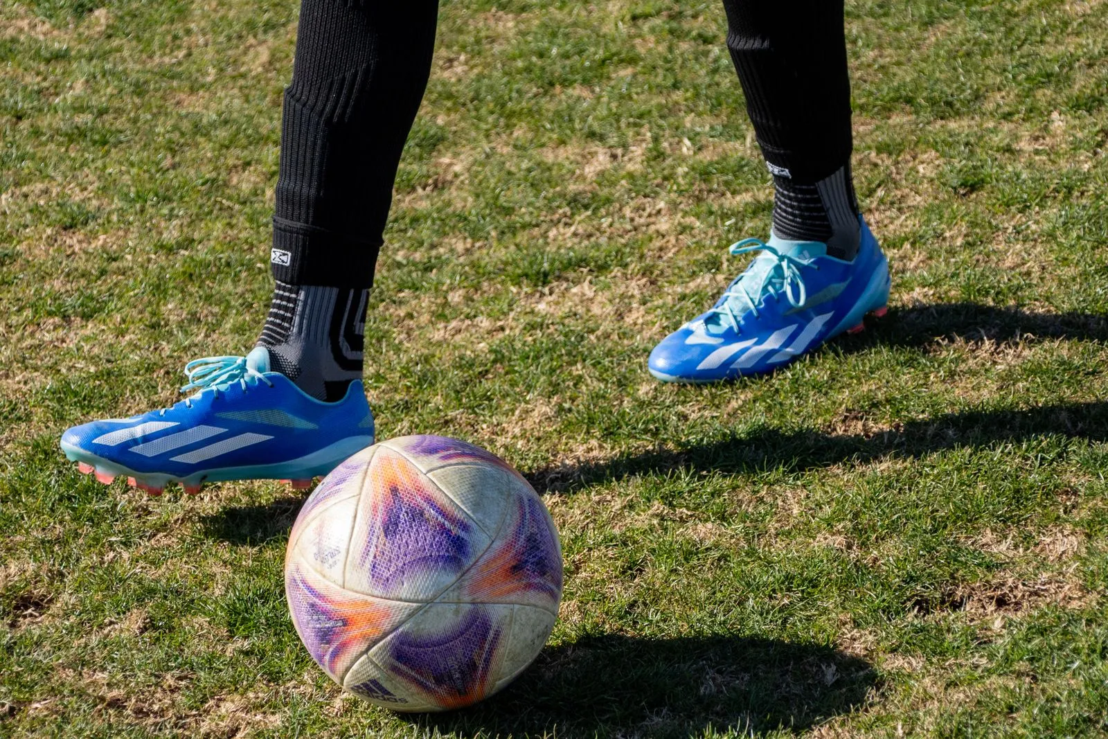 Close-up of a soccer player's feet in blue cleats on a grassy field with a colorful soccer ball.